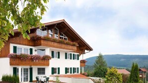 Un bâtiment à deux étages doté d’un balcon, d’un coin repas avec des chaises et offrant une vue sur les montagnes en arrière-plan.