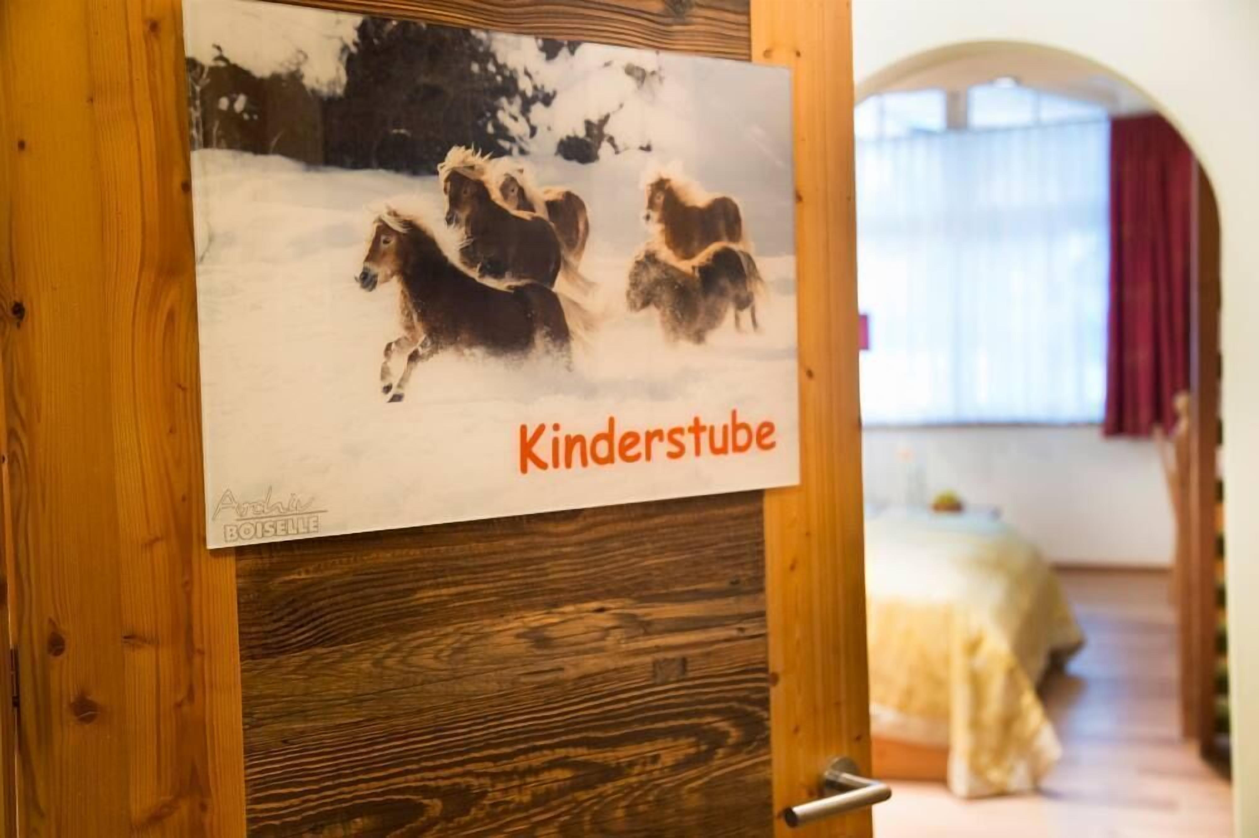 Eine Holztür mit einem Poster von Pferden in einer verschneiten Landschaft und dem Text "Kinderstube".