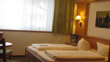 A hotel room with two single beds, a wooden headboard, a desk with a chair, a lamp, and a painting on the wall.