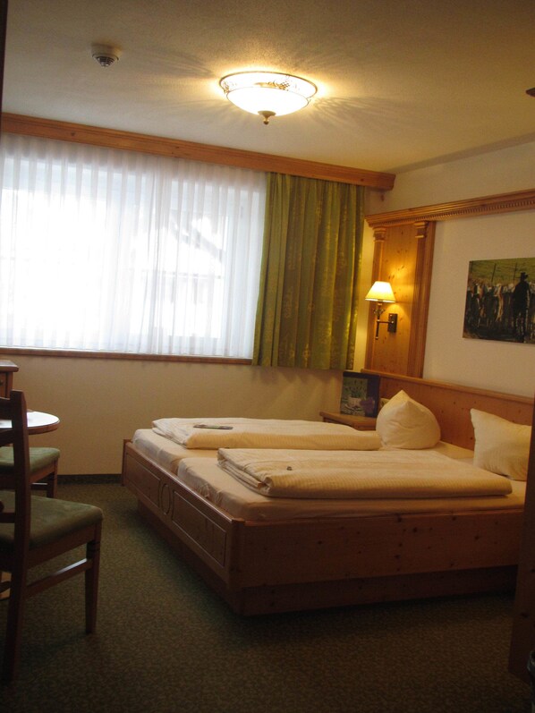 A hotel room with two single beds, a wooden headboard, a desk with a chair, a lamp, and a painting on the wall.