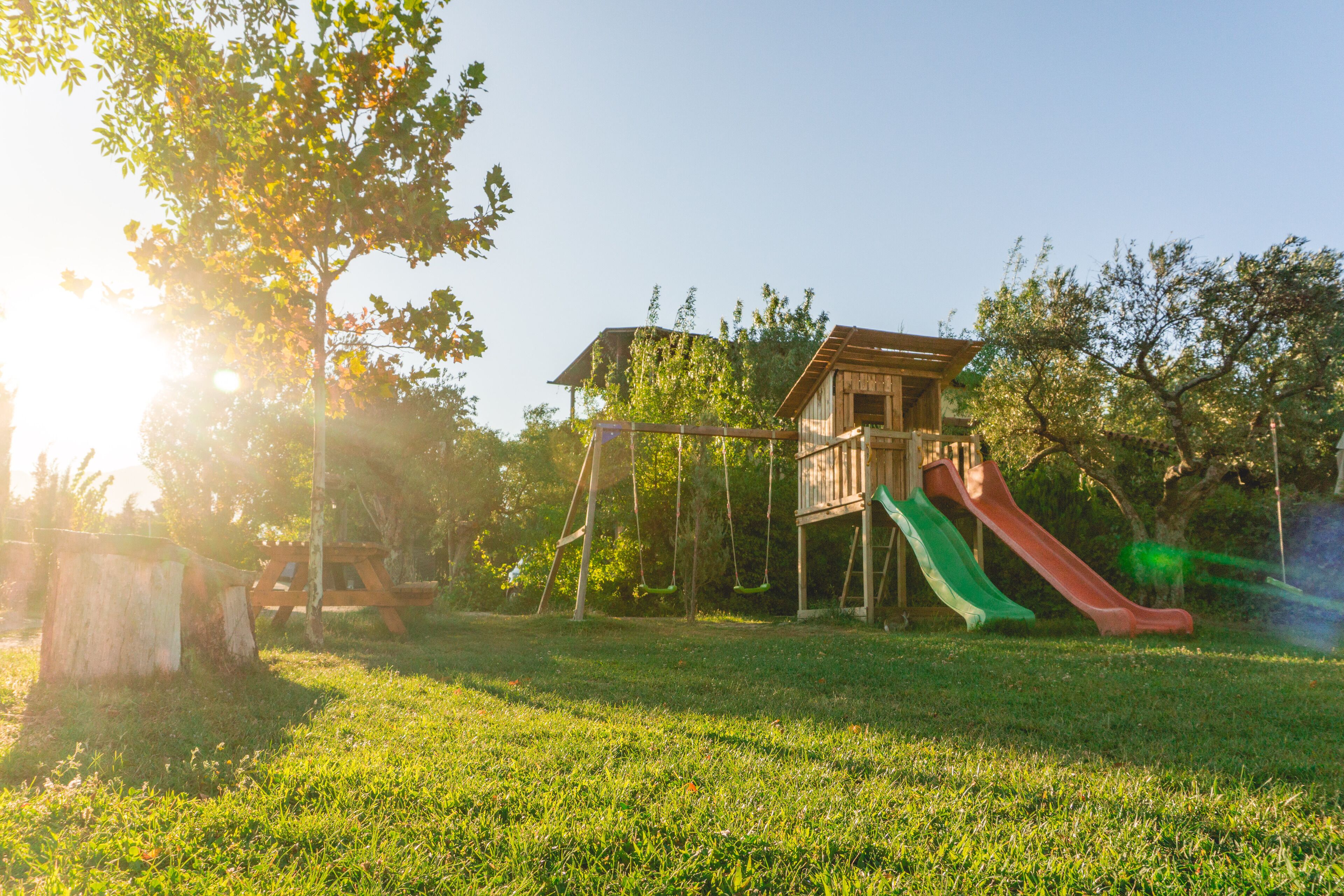 Une aire de jeux avec des toboggans et des balançoires, entourée d’arbres et agrémentée d’une structure en bois.