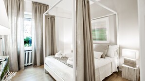 A modern bedroom with a four-poster bed, beige curtains, and a bedside table with a lamp. - The best in Rome PRESTIGE VINE  (Roma)