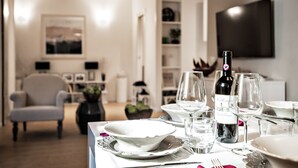 A dining table set with white plates, glasses, and a bottle of wine, with a modern interior including a chair and a TV in the background. - The best in Rome PRESTIGE VINE  (Roma)