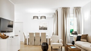 A modern living room with a white sofa, a dining table with chairs, a TV, and a black vase. - The best in Rome PRESTIGE VINE  (Roma)