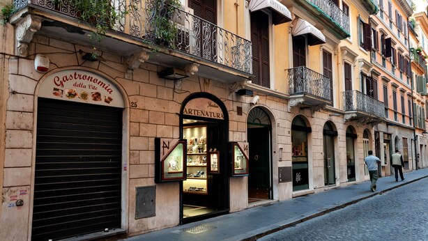 A multi-story building with balconies, a storefront with a sign, and a cobblestone street. - The best in Rome PRESTIGE VINE  (Roma)
