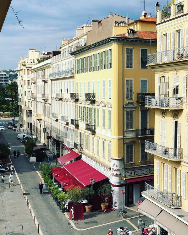 A row of yellow buildings with balconies, a red awning, and a sign for 'La Petite Maison'.