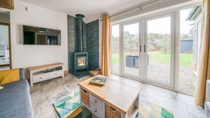 Ein modernes Wohnzimmer mit Kamin, Fernseher und einer großen Glasschiebetür, die zu einem Außenbereich führt.
