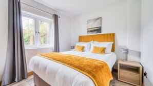 Ein Schlafzimmer mit einem großen Bett, einem Nachttisch, einem Fenster mit Vorhängen und einem Bild an der Wand.