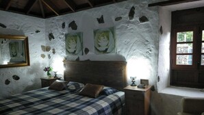 A bedroom with a bed, a nightstand, a chair, a window, and stone walls. - Rural house (full rental) Finca Los Ciruelos for 2 people (Icod de los Vinos)