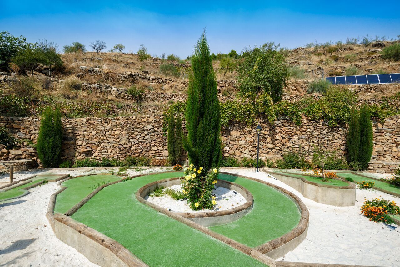 A golf course with sand bunkers, a stone wall, and solar panels in the background.