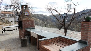 Cocina exterior con horno de piedra, lavaplatos y vistas a las montañas.