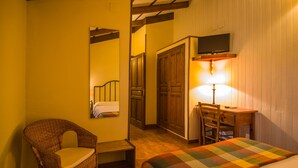 Una habitación de hotel con cama, una silla de mimbre, un escritorio y un televisor.