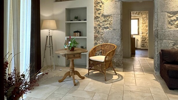 A room with a stone wall, a wooden table with a chair, a lamp, and a sofa. - Rural House La Casa dels Avis (Ullà)