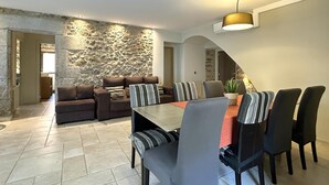 A dining area with a stone wall, a sofa set, and a dining table with chairs. - Rural House La Casa dels Avis (Ullà)