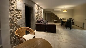 A cozy living area with stone walls, a wooden dining table, and comfortable seating. - Rural House La Casa dels Avis (Ullà)