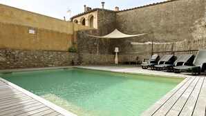 A pool area with a wooden deck, lounge chairs, and a stone wall. - Rural House La Casa dels Avis (Ullà)