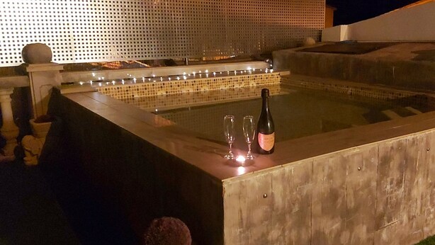 Un bain à remous avec un bord en bois, une bouteille et deux verres posés dessus.