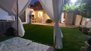 Un espace patio agrémenté d’une pelouse verdoyante, d’un mur en pierre et d’un coin salon avec des coussins.