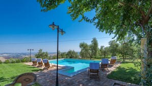 Ein Swimmingpool mit Liegestühlen und einer Pergola, umgeben von einer Rasenfläche und Bäumen.