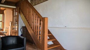 Un escalier en bois menant à l’étage supérieur, un canapé en cuir noir et un sol carrelé.