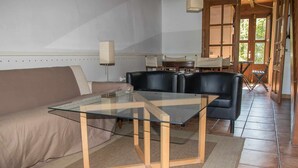 Un salon moderne avec une table à plateau en verre, des fauteuils en cuir, un canapé beige et un plancher en bois.
