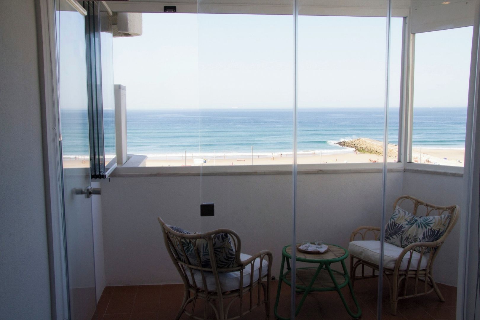 Ein Balkon mit Blick auf den Strand, mit Korbstühlen und einem kleinen Tisch.