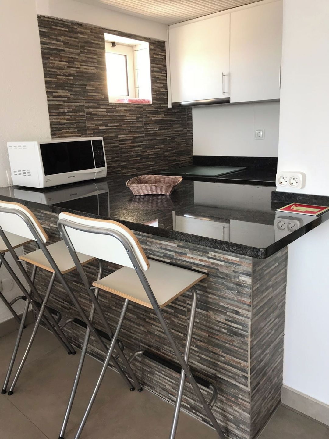 A kitchen with a microwave, a sink, and a counter with chairs.