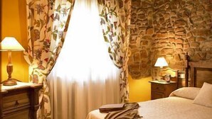 A bedroom with a stone wall, a bed with a blanket, a nightstand with a lamp, and a wooden dresser. - Rural apartment El Mirador de Cazanes for 4 people (Villaviciosa)