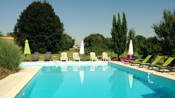 Piscina con sillas de descanso y sombrillas, rodeada de árboles y vegetación.