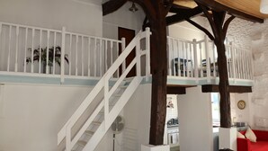 Una escalera con barandillas blancas que sube a una zona de entrepiso, un sofá rojo y una cocina visible al fondo.