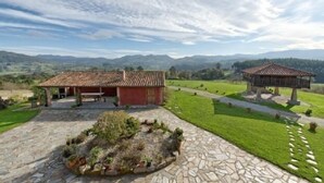 A rural house with a stone pathway leading to a red-roofed building, surrounded by green fields and mountains in the background. - Rural apartment El Mirador de Cazanes for 2 people (Villaviciosa)