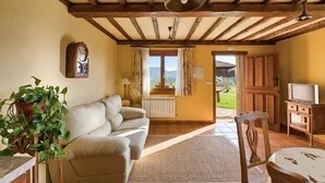 A cozy living room with a sofa, a wooden ceiling, a clock, a TV, and a view of the outdoors. - Rural apartment El Mirador de Cazanes for 2 people (Villaviciosa)