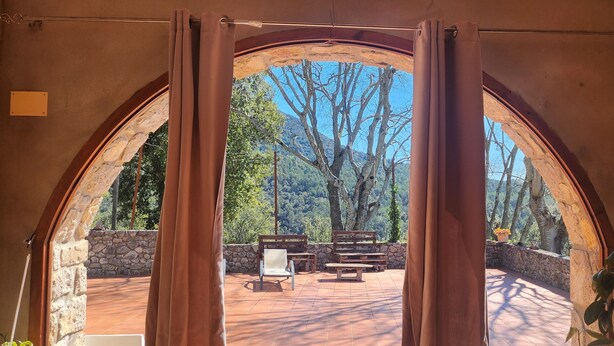 An arched doorway leading to an outdoor patio with stone walls, wooden furniture, and a view of trees and hills. - Self catering Can Servosa for 11 people (Sales de Llierca)