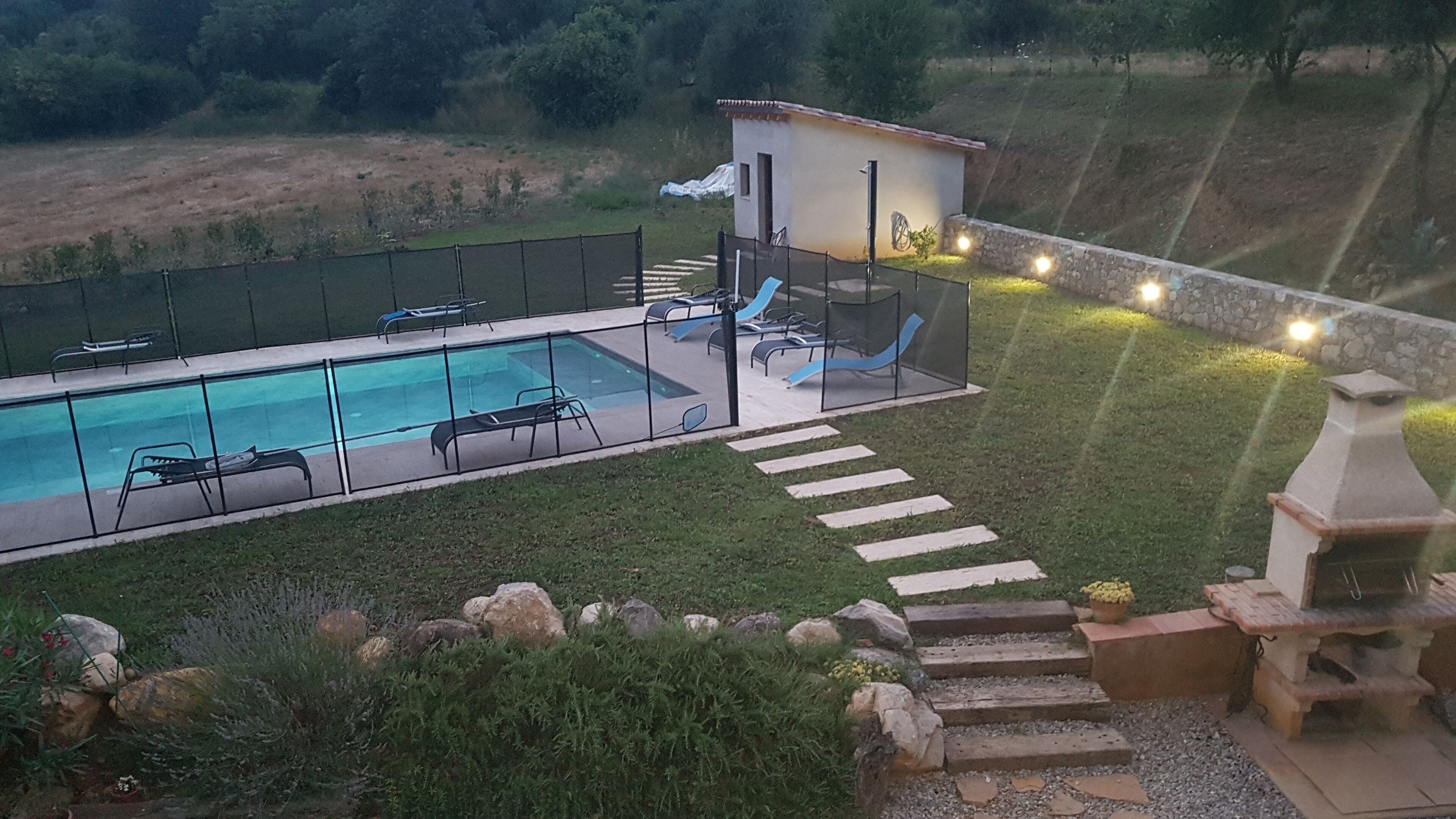 A swimming pool with lounge chairs and a slide, surrounded by a fenced deck and a small building.