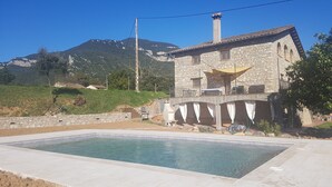A stone house with a swimming pool, a balcony, and a mountain backdrop. - Self catering Can Servosa for 11 people (Sales de Llierca)