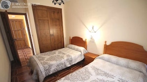 Quarto com duas camas, um guarda-roupa de madeira e chão de azulejos.