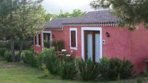 A red building with a tiled roof, a door, and a small table with chairs in the front yard. - L'AGLIENTU CALLA ROOM (Loiri)