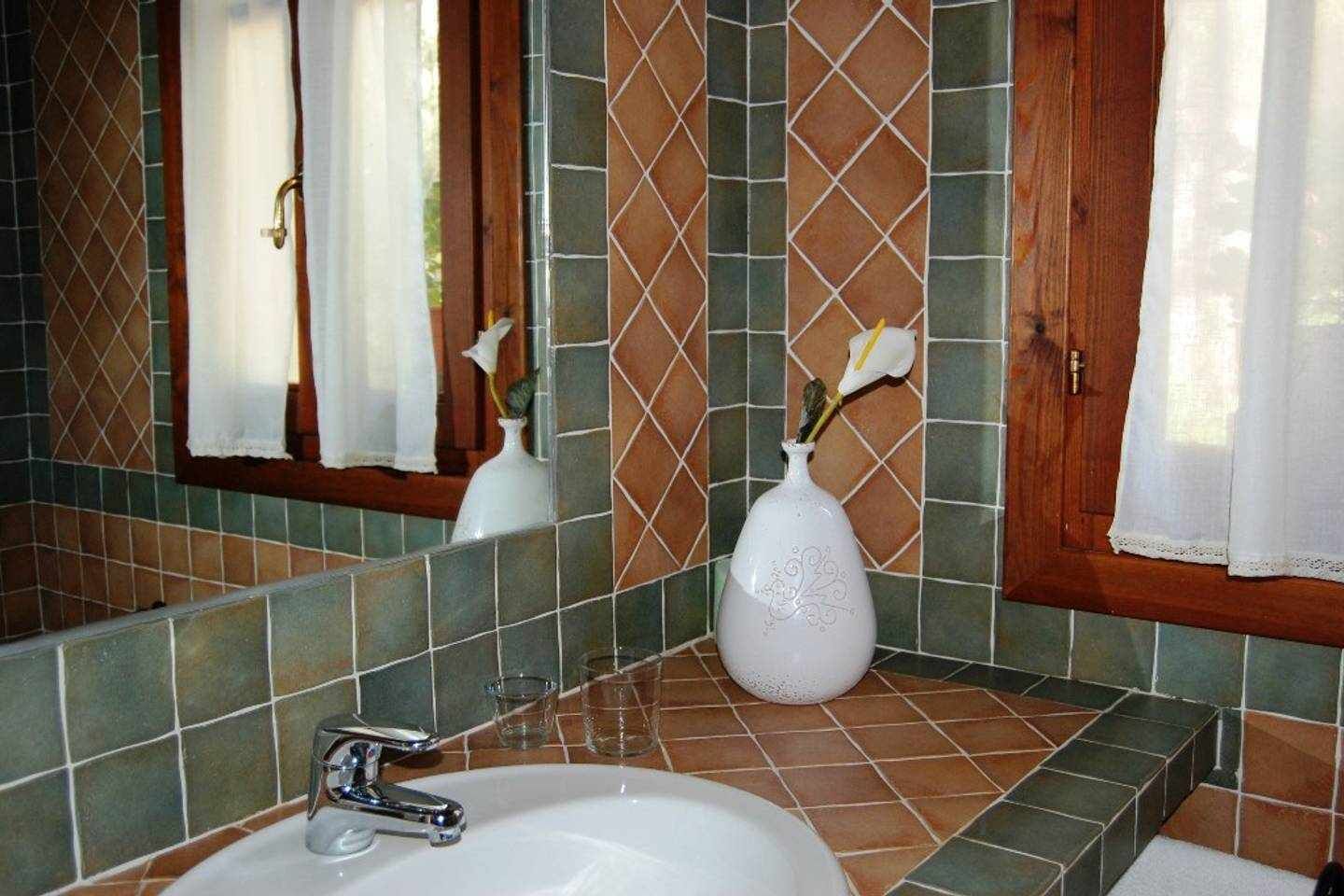 Un baño con lavamanos, espejo y dos jarrones con flores.