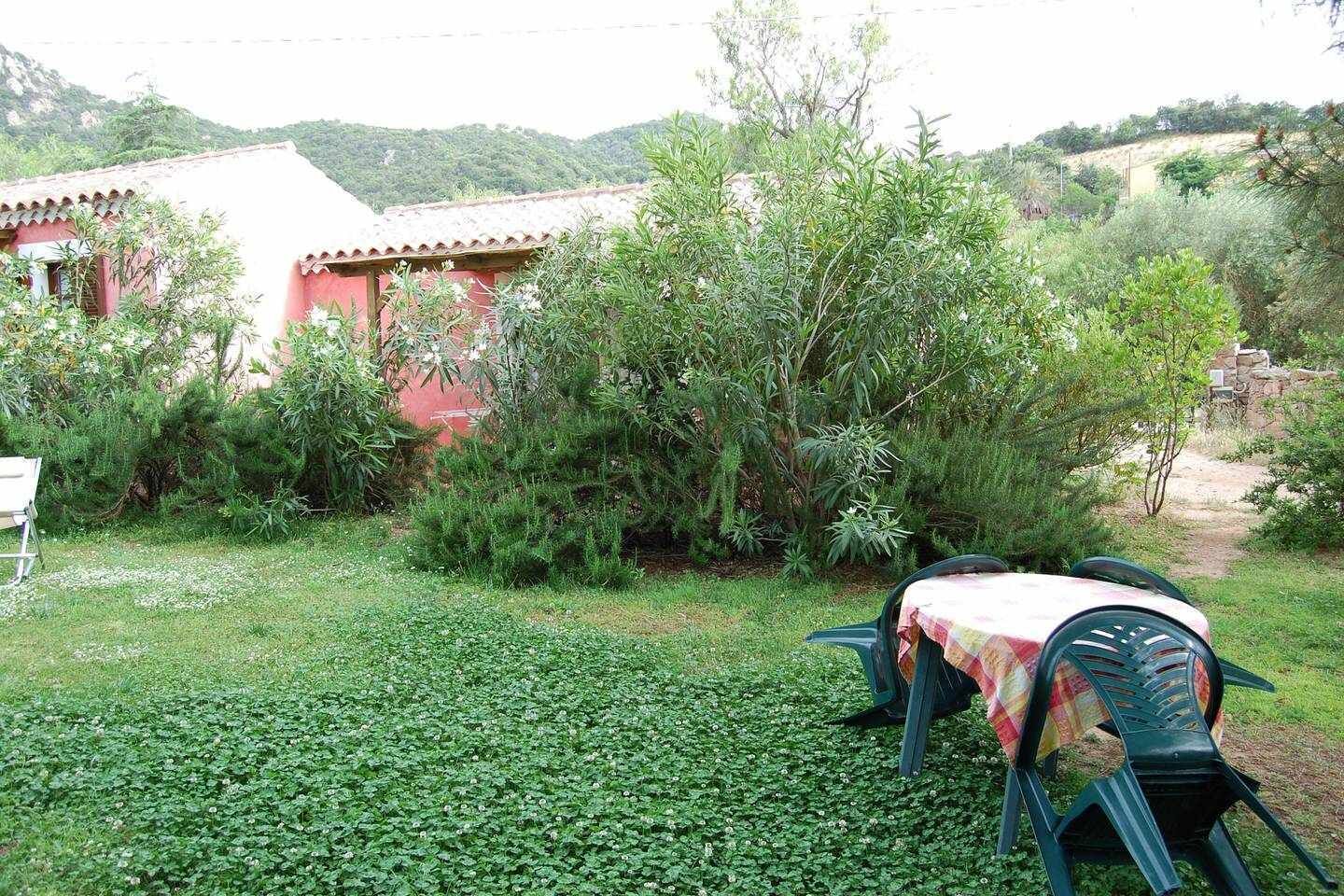 Un patio con mesa y sillas, rodeado de follaje y un edificio de fachada roja.