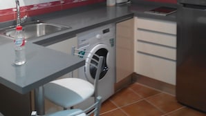 Ett litet kök med tvättmaskin, diskho och mikrovågsugn.