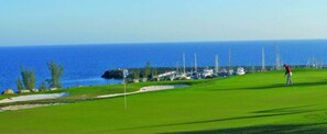 Ein Golfplatz mit Blick auf das Meer und Boote im Hintergrund.