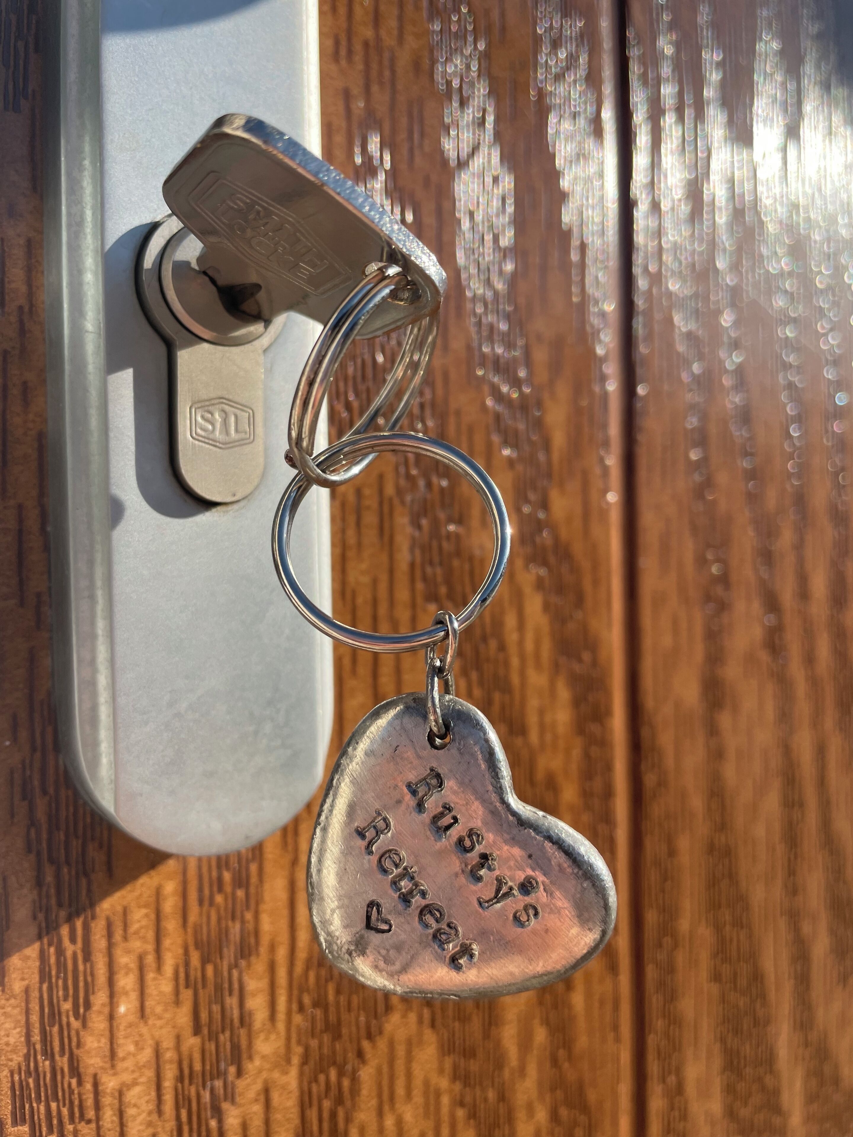 Een sleutelhanger met een hartvormige bedel, bevestigd aan een sleutelring, hangend op een metalen oppervlak.