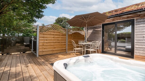 Un jacuzzi con una terraza de madera, una mesa con sillas y un área de patio techada.