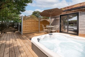 Un jacuzzi con una terraza de madera, una mesa con sillas y un área de patio techada.