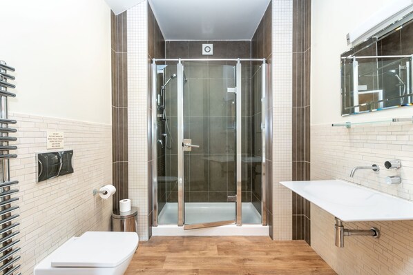 Un baño moderno con ducha de vidrio, lavamanos blanco y retrete.
