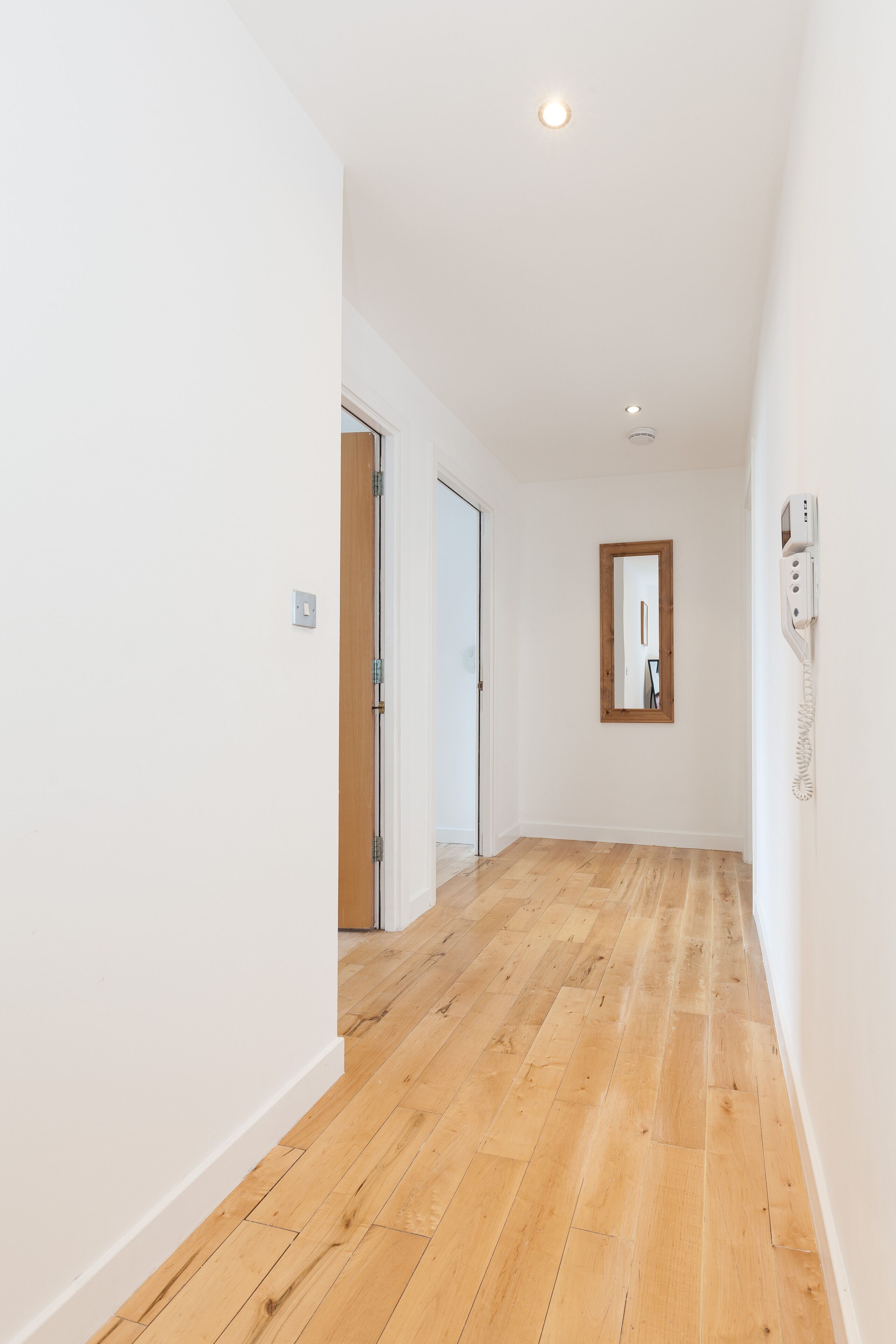 Un couloir avec un plancher en bois, des murs blancs et une porte au fond.