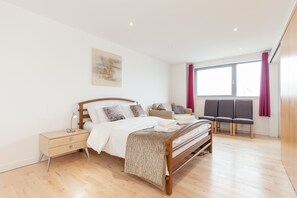 Ein Schlafzimmer mit einem hölzernen Bett, einem Nachttisch, einem Fenster mit Vorhängen und einer Sitzecke mit Stühlen.