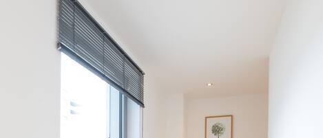 A hallway with a window, a potted plant, a framed mirror, and a wall-mounted picture.