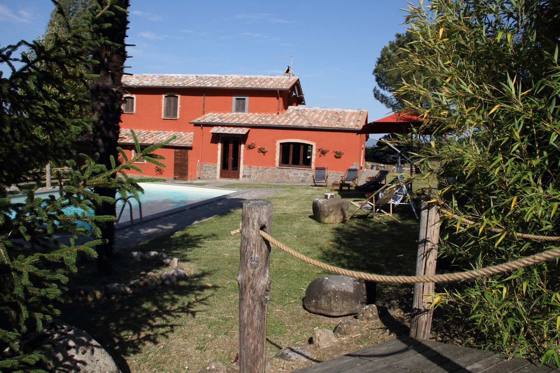 A red building with a tiled roof, a swimming pool, and outdoor seating.