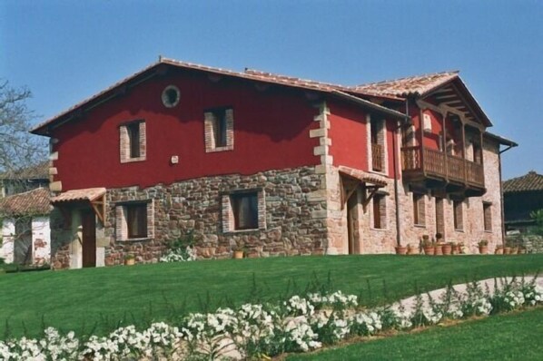 A two-story stone house with a red facade and a balcony.